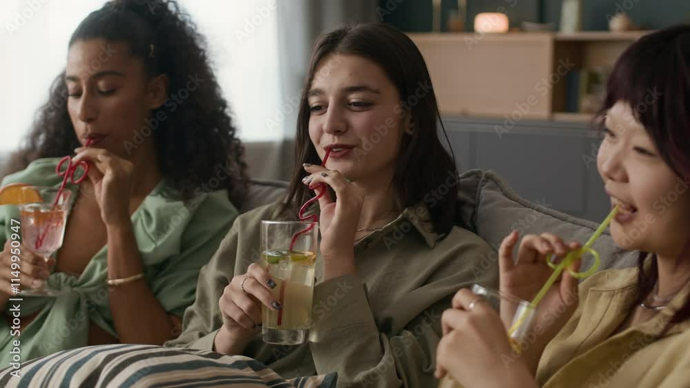Handheld shot of cheerful multi-ethnic female zoomers celebrating with soft drinks and chatting during home party