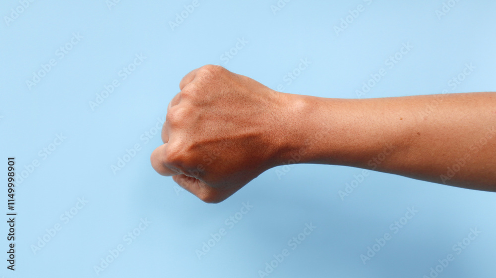 Powerful male clenched fist isolated on a blue background, representing strength, determination, and empowerment. Powerful male clenched fist isolated on a blue background, representing strength, determination, and empowerment.