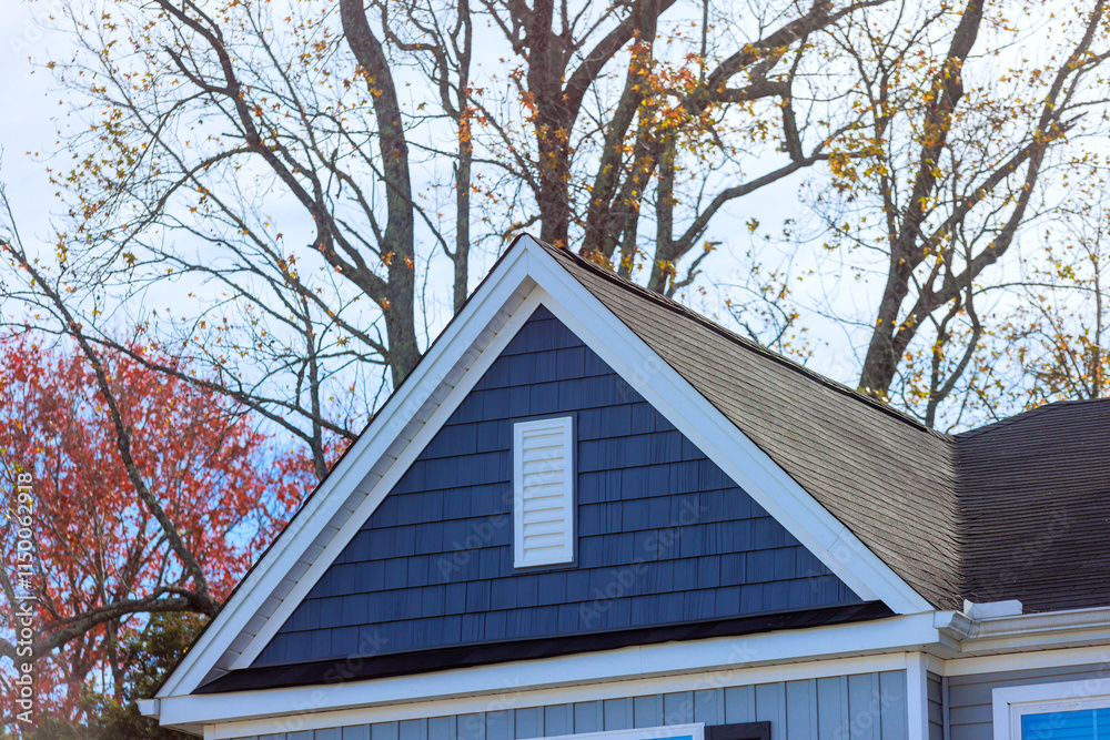Blue vinyl siding in house framed by autumn trees displaying vibrant sunlight illuminates structure beautifully. Blue vinyl siding in house framed by autumn trees displaying vibrant sunlight illuminates structure beautifully.