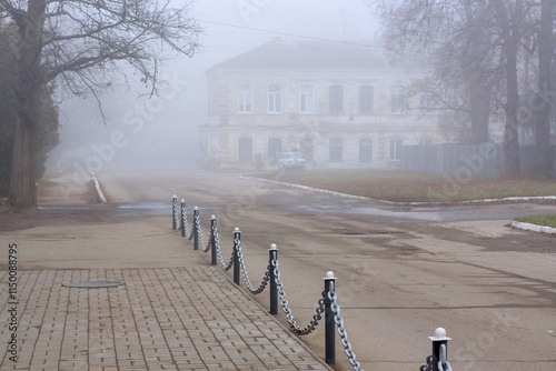 oggy street with asphalt sidewalk, chain link fences and old two-story house in the background. Atmospheric cityscapes. photo