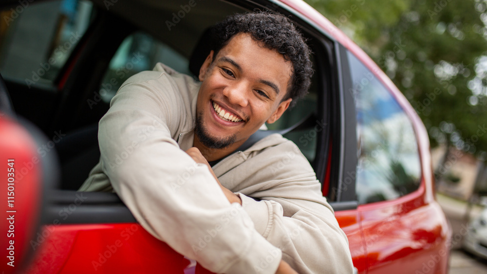 Obraz premium Young man smiling in red car with open window