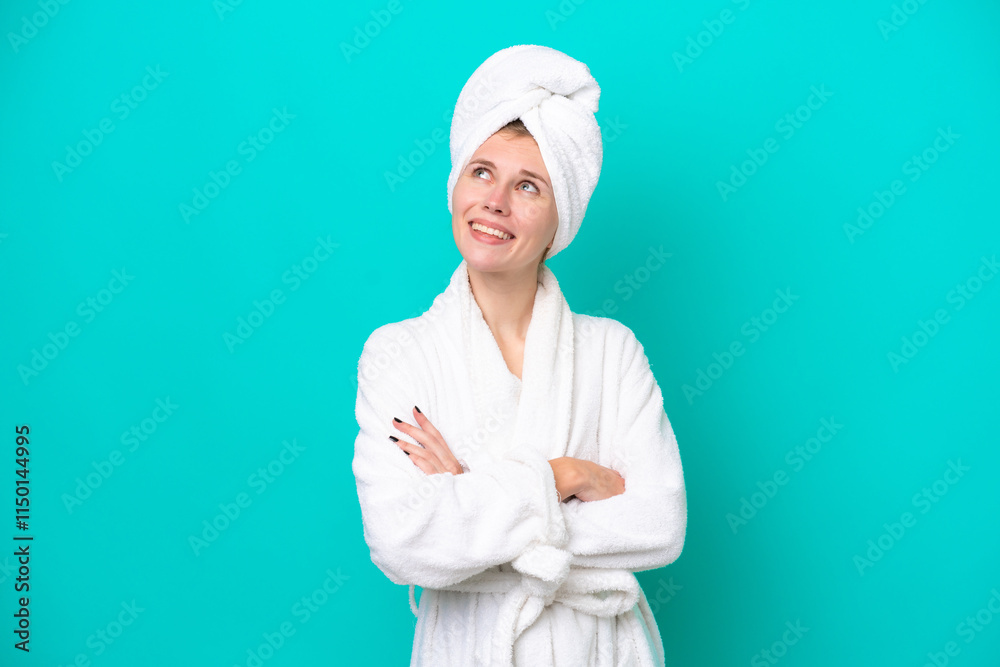 Young woman in a bathrobe isolated on blue background looking up while smiling Young woman in a bathrobe isolated on blue background looking up while smiling