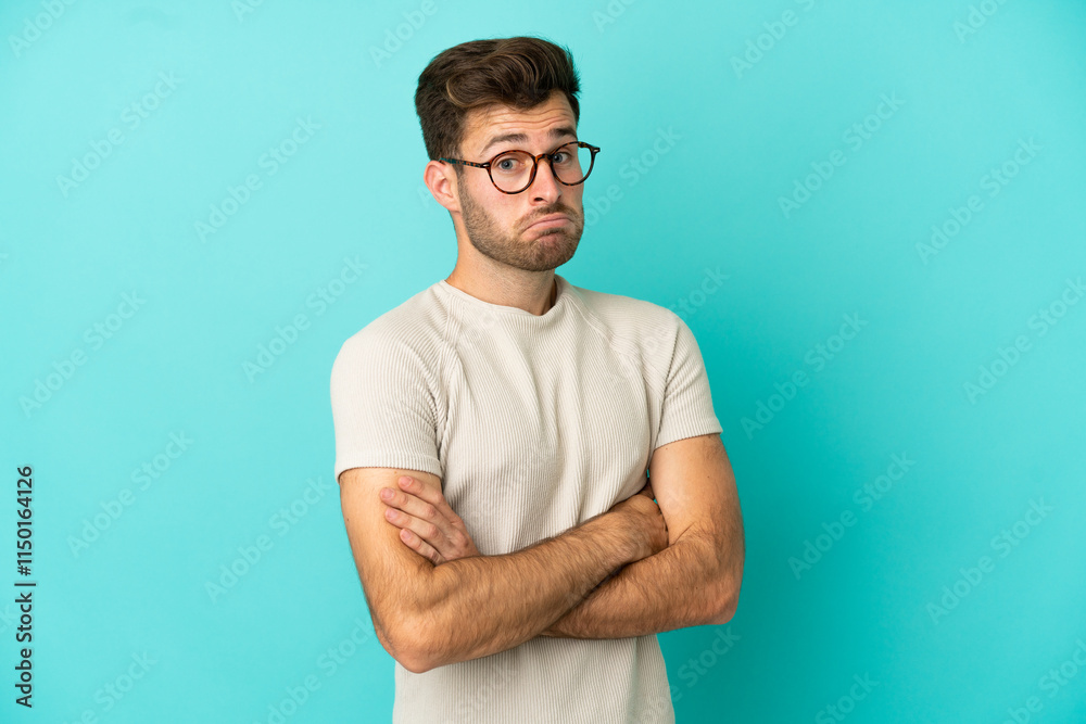 Young caucasian handsome man isolated on blue background making doubts gesture while lifting the shoulders
