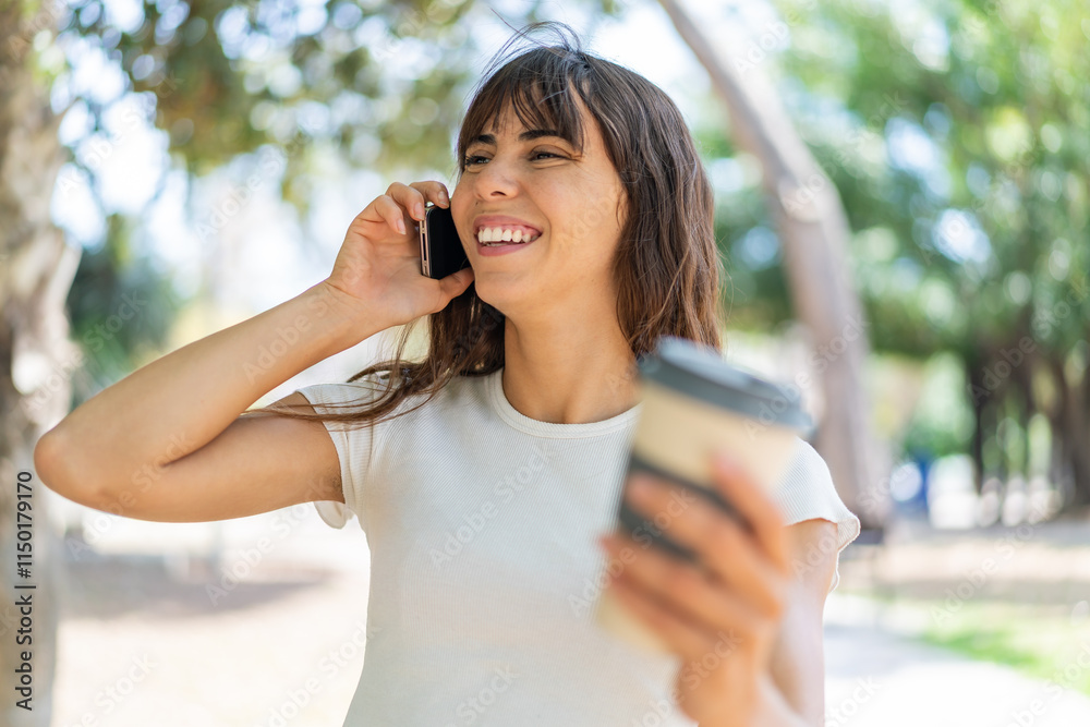 Young woman at outdoors using mobile phone and holding a coffee with happy expression Young woman at outdoors using mobile phone and holding a coffee with happy expression