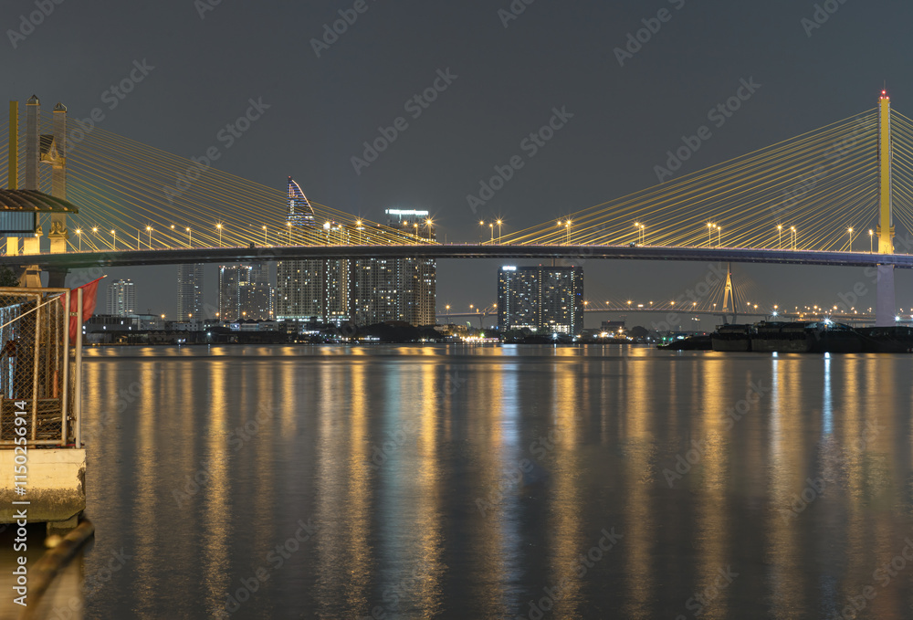 Night view after sunset of Thotsamarachan Bridge (Rama IX Bridge) crossing Chao phraya river with skyscraper in the background. Beautiful city of Bangkok with bright glowing lights in the sundown,