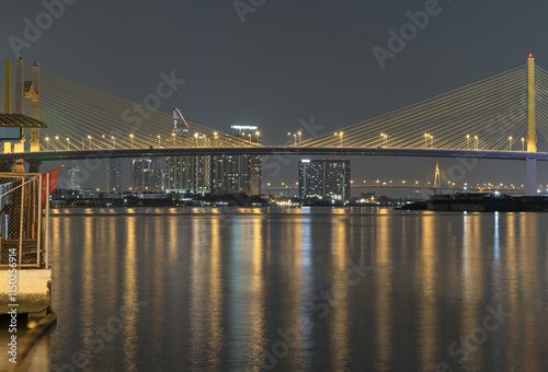 Obraz na płótnie Night view after sunset of Thotsamarachan Bridge (Rama IX Bridge) crossing Chao phraya river with skyscraper in the background. Beautiful city of Bangkok with bright glowing lights in the sundown, w salonie