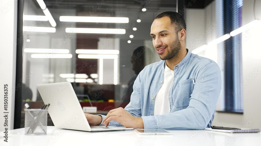 Young african american businessman working on laptop in modern office, smiling while typing. Black man employee using computer application, banking, texting client, chatting online. busy with project