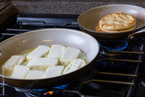 A pan of cheese is cooking on a stove and pitta bread warming up in the background. photo