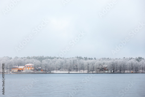 Swedish white winter snow landscape over calm water with Nedre Manilla orange villa on Djurgården, Stockholm, by the waterfront photo