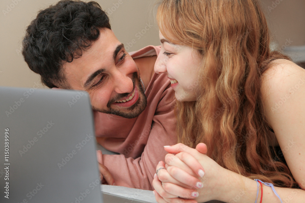 young cheerful couple using laptop in the bedroom lying down relaxing, watching movie, shopping online young cheerful couple using laptop in the bedroom lying down relaxing, watching movie, shopping online