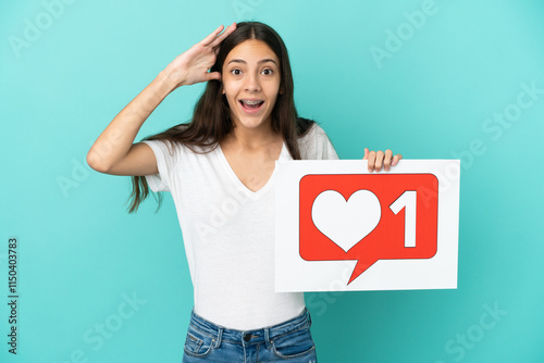 Young French woman isolated on blue background holding a placard with Like icon with surprised expression photo