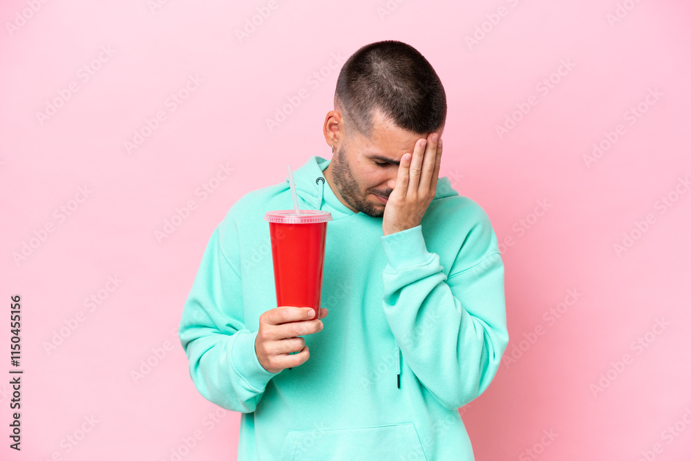 Young caucasian man holding soda isolated on pink background with tired and sick expression Young caucasian man holding soda isolated on pink background with tired and sick expression