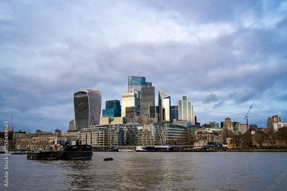 Naklejka premium London’s modern skyline viewed from the Thames River, featuring iconic skyscrapers like the Walkie-Talkie and the Gherkin under a cloudy sky. London district Stock photo