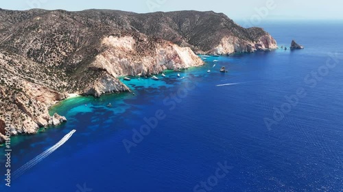 Aerial drone cinematic video of paradise blue bay of uninhabited island of Polyaigos with turquoise crystal clear sea visited by luxury yachts and sail boats resembling a blue lagoon, Cyclades, Greece photo