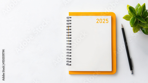 2025 Goal Setting Concept. Blank notepad with orange cover, pen, and a plant on a white surface.