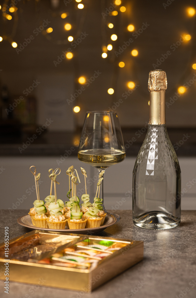On a plate on the kitchen table there are tartlets with salad and fresh cucumber, next to there is a bottle of champagne and a selection of sweets. Vertical photo On a plate on the kitchen table there are tartlets with salad and fresh cucumber, next to there is a bottle of champagne and a selection of sweets. Vertical photo