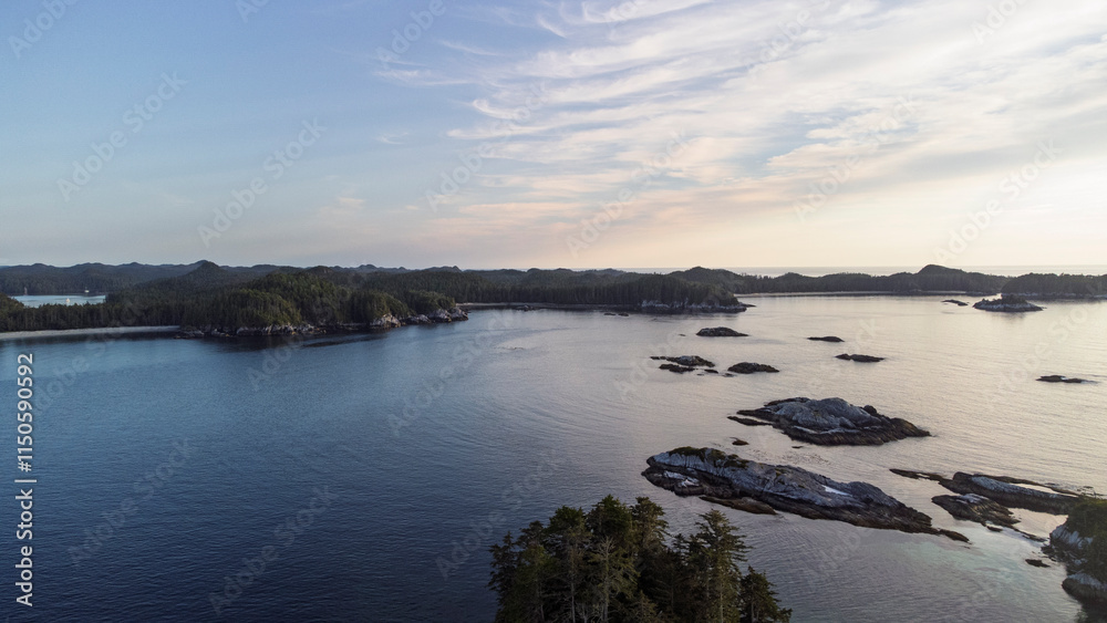 Obraz premium Small islands sit in a the calm ocean as the yellow light of the sun setting creeps across the sky. 