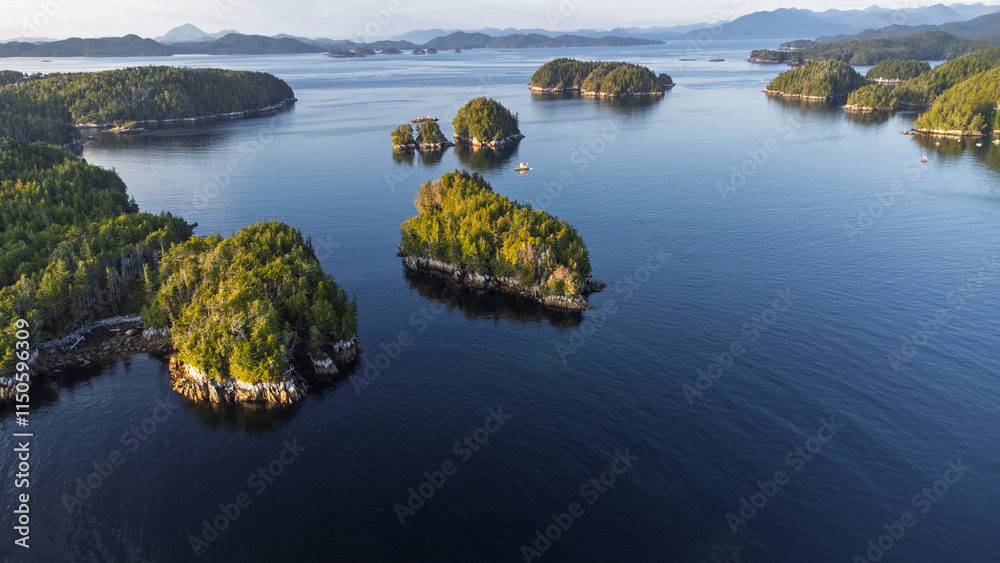 Heavily forested islands dot a narrow straight on a calm day with mountains in the background. Taken near Calvert Island, British Columbia, Canada Heavily forested islands dot a narrow straight on a calm day with mountains in the background. Taken near Calvert Island, British Columbia, Canada