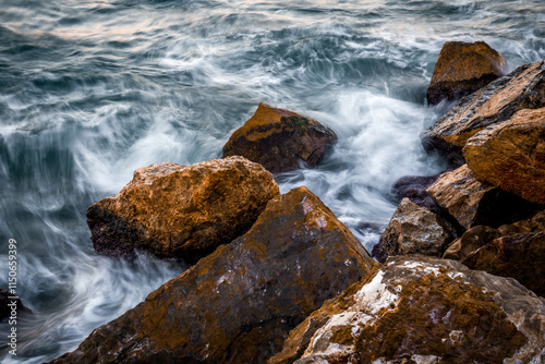 Close-up of stones on the coast with the sea with silky effect at sunset. Low shutter speed photo