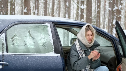 woman drinks hot tea while sitting in a car in a winter forest