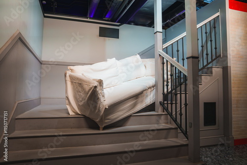A white couch is positioned on a staircase with a wooden railing, part of a Friends themed exhibition in London, replicating a famous TV scene.