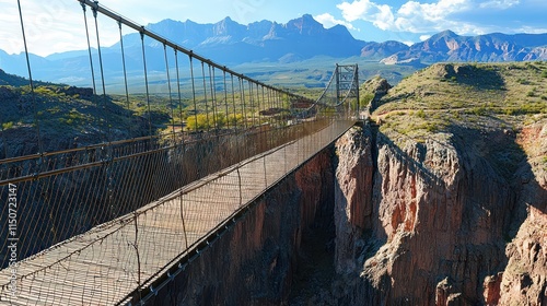 Pedestrian suspension bridge crossing a deep canyon, with mountains towering in the distance