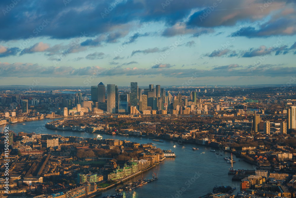 Fototapeta premium Aerial view of London's Canary Wharf skyline with modern skyscrapers. The River Thames reflects the warm glow of the setting sun during Christmas.