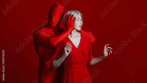 External and internal condemnation. Public opinion closes my ears to my needs. A feminist concept. Mysterious red hands surround and cover the ears of a woman in red, a photo on a red background.