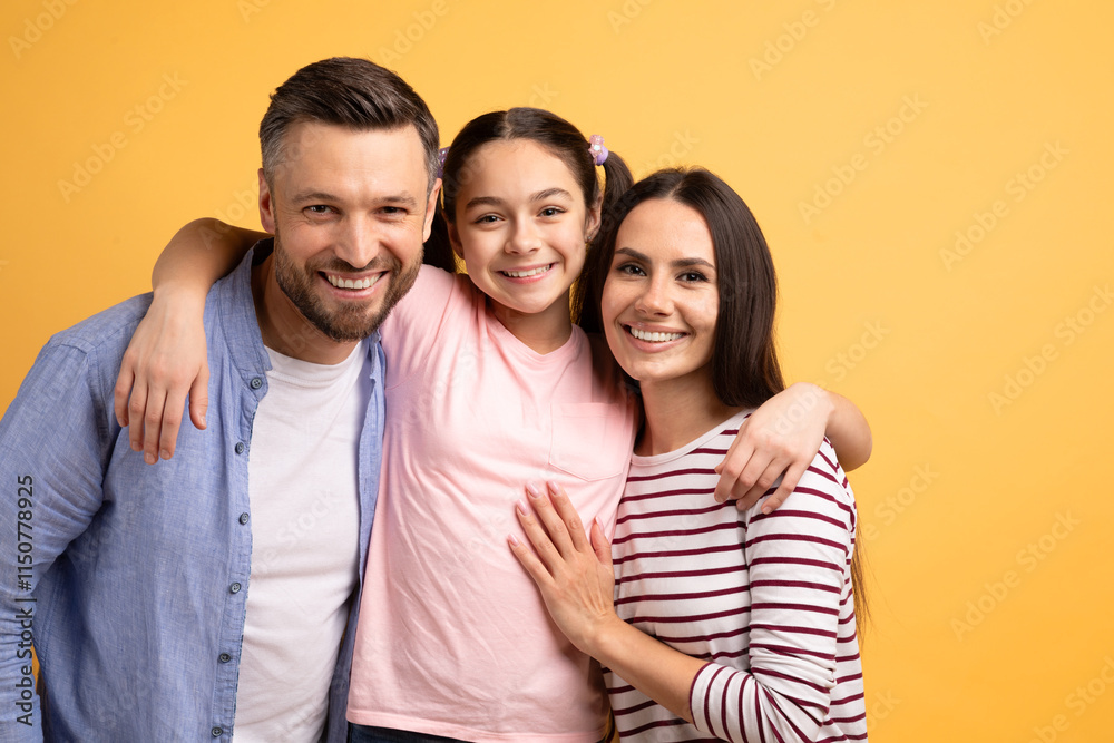 Obraz premium A Caucasian mother, father, and their teenage daughter share a joyful embrace against a bright yellow backdrop, showcasing their strong bond and affection for one another.