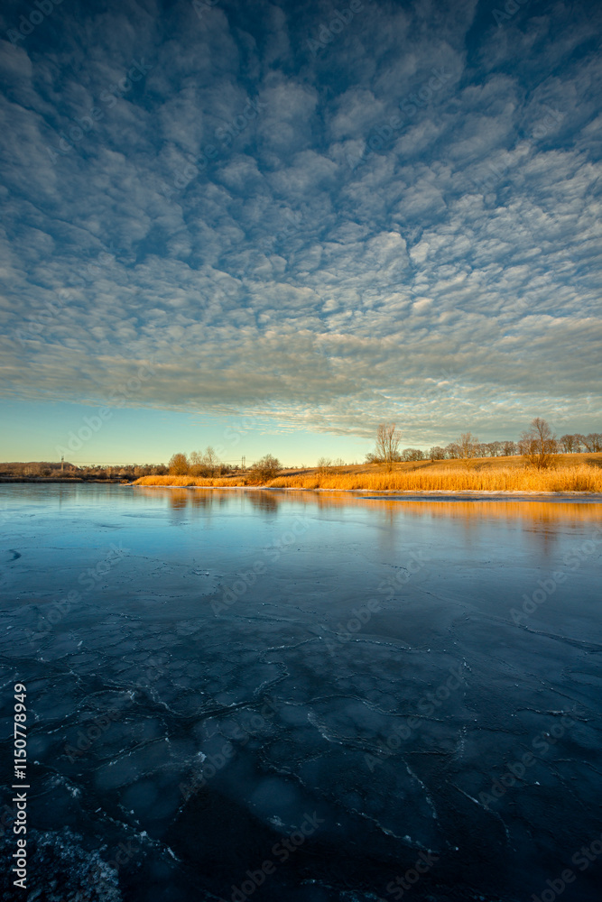 Naklejka premium Frozen sea at the winter ,morning on the pon, frozen water.Landscape with beautiful lake .Winter time , beautiful sunrise over the trees , smooth and big clouds in the sky, snow on the beach with reed