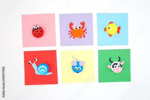 DIY plastic bottle caps for crafts and art project, colored paper on a white background. Flat lay composition with fish, cow, ladybug, mouse, crab, and snail designs. DIY activity, recycling concept, photo