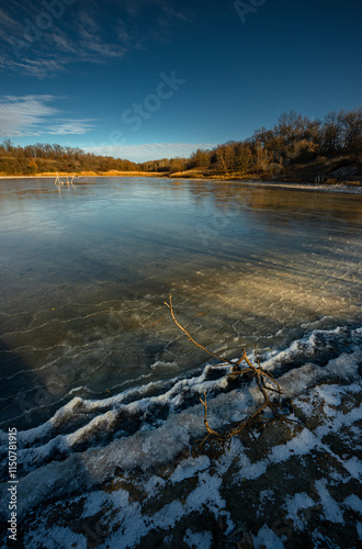 Feozen pond at the winter day,lake with ice,dry ground near the lake.Sun in the sky, sunlights and sky with blue clouds.Blue winter colors , wild nature with a pond.Frozen beach near the lake,snowy  photo