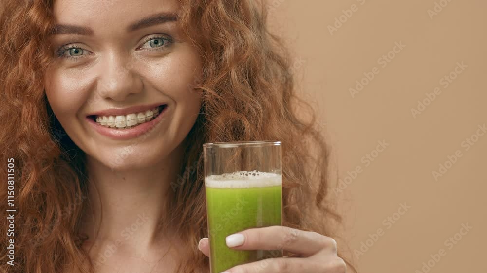 A cheerful woman with curly hair enjoys a refreshing green juice, radiating positivity. The warm background complements her bright smile and healthy beverage choice.