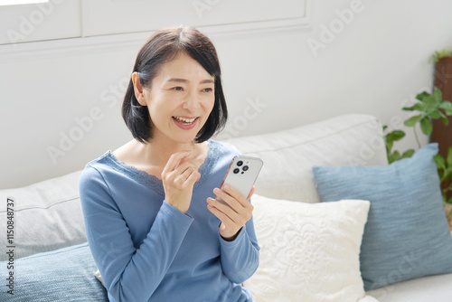 スマホを持つ中年女性　リビング