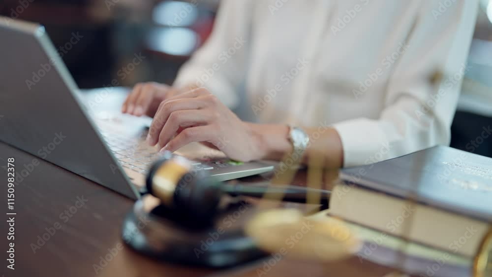 A woman is typing on a laptop in front of a gavel. The gavel is on a desk next to a book A woman is typing on a laptop in front of a gavel. The gavel is on a desk next to a book