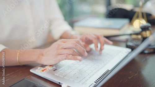 A woman is typing on a laptop computer. She is wearing a white shirt and has a watch on her wrist. The laptop is on a wooden table