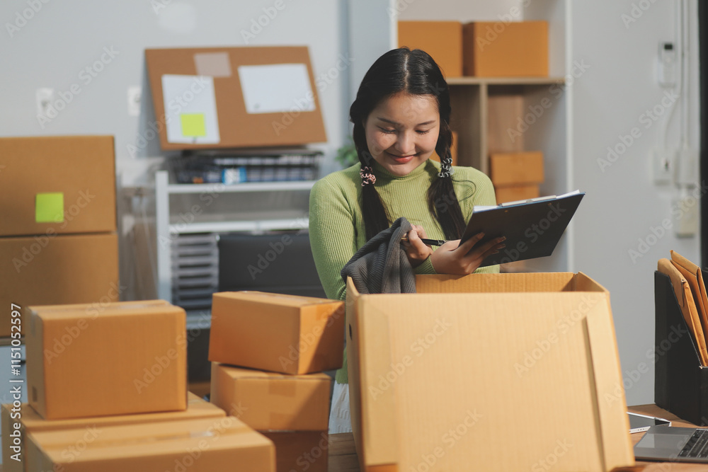 Startup SME small business entrepreneur of freelance Asian woman wearing apron using laptop and box to receive and review orders online to prepare to pack sell to customers, online sme business ideas. Startup SME small business entrepreneur of freelance Asian woman wearing apron using laptop and box to receive and review orders online to prepare to pack sell to customers, online sme business ideas.