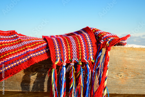 ceinture fléchée (traditional pattern) replica of the woven sash worn by voyageurs during the fur trade shot outside on a wooden dock in the sun with snow room for text
