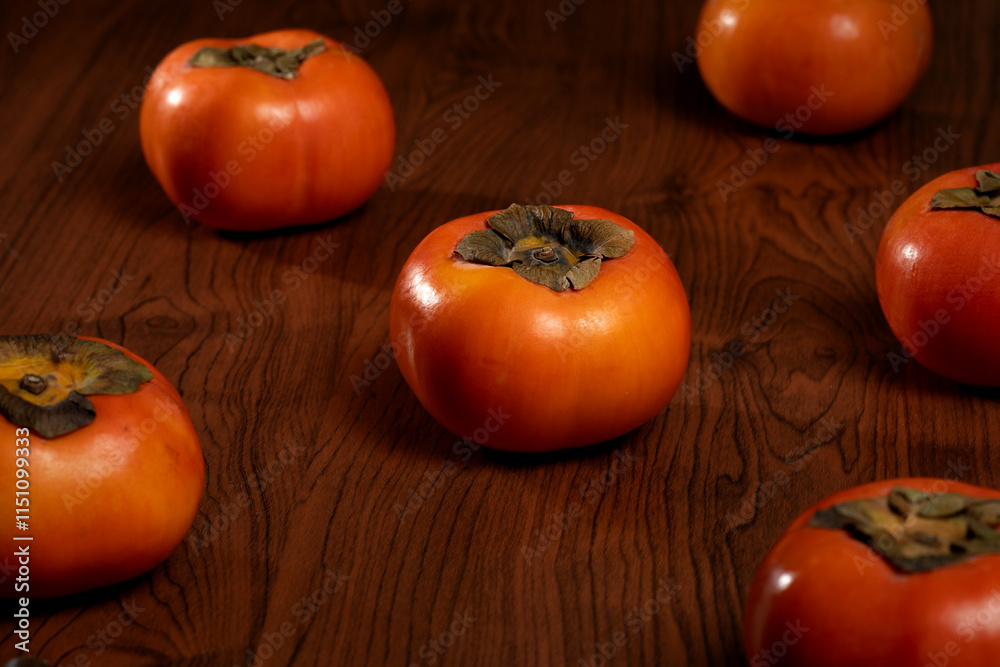 A rustic wooden tray filled with vibrant, ripe persimmons, their orange skin smooth and glossy. A rustic wooden tray filled with vibrant, ripe persimmons, their orange skin smooth and glossy.