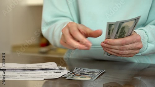 Woman counts us dollar banknotes on a table, surrounded by receipts. The scene captures the meticulous handling of cash, reflecting financial management and budgeting practices