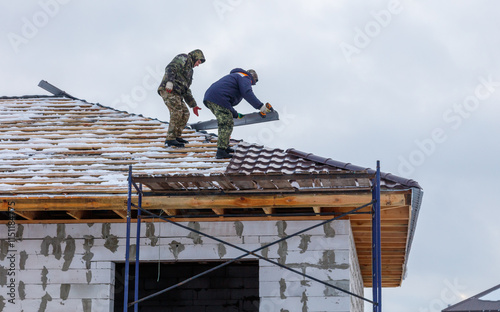 Two men are working on a roof, one of them is wearing a blue jacket photo