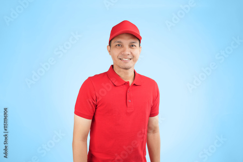 A cheerful Asian delivery worker in a red uniform and cap stands against a blue background, showcasing a friendly and professional demeanor ideal for customer-focused services.