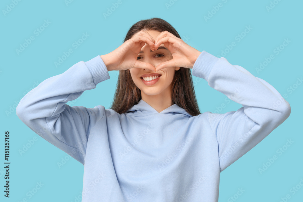 Beautiful young woman making heart gesture on blue background