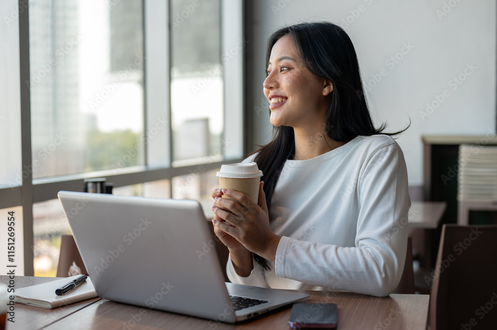 An Asian woman enjoying a hot drink at a coffee shop while taking a break from work on her laptop. An Asian woman enjoying a hot drink at a coffee shop while taking a break from work on her laptop.