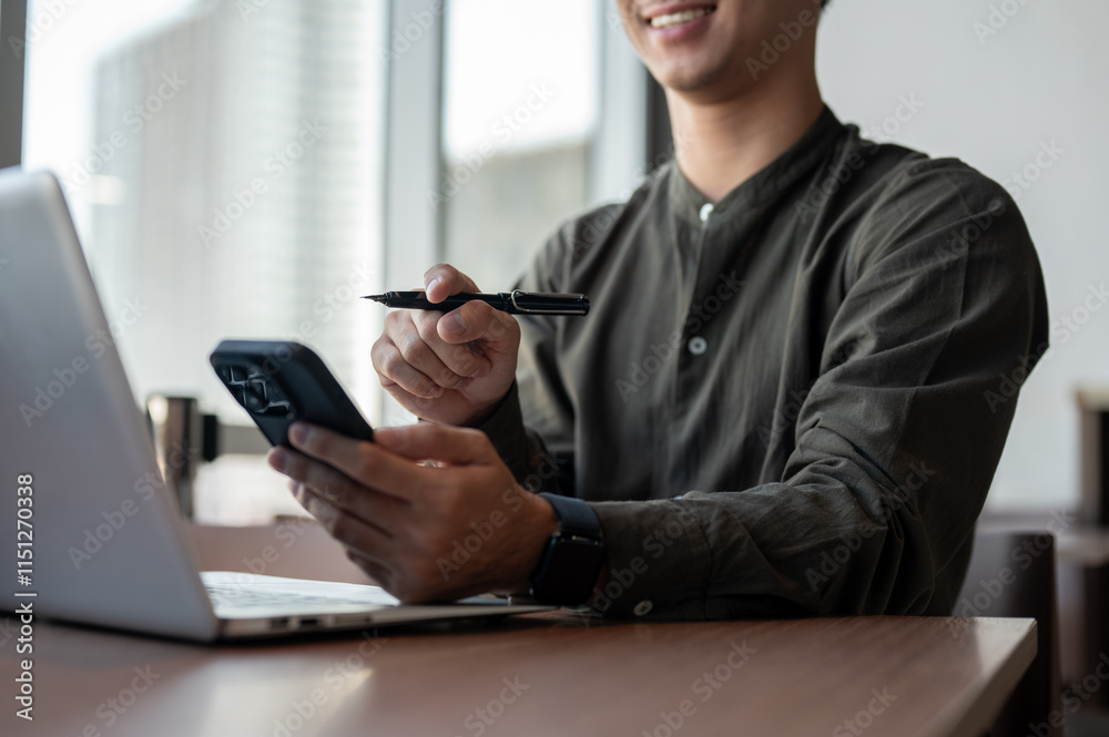 A close-up of an Asian businessman using his smartphone while working in a modern office. A close-up of an Asian businessman using his smartphone while working in a modern office.