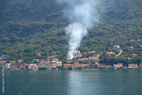 Smoke plume over peaceful mountain village scene.