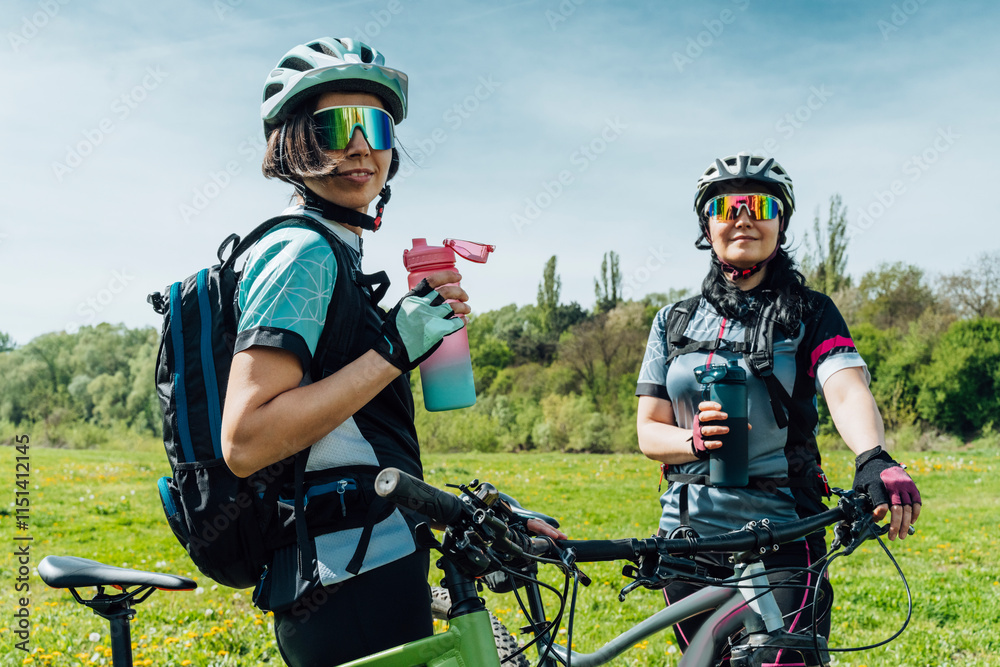 Friends with bottle and cycle standing at meadow Friends with bottle and cycle standing at meadow