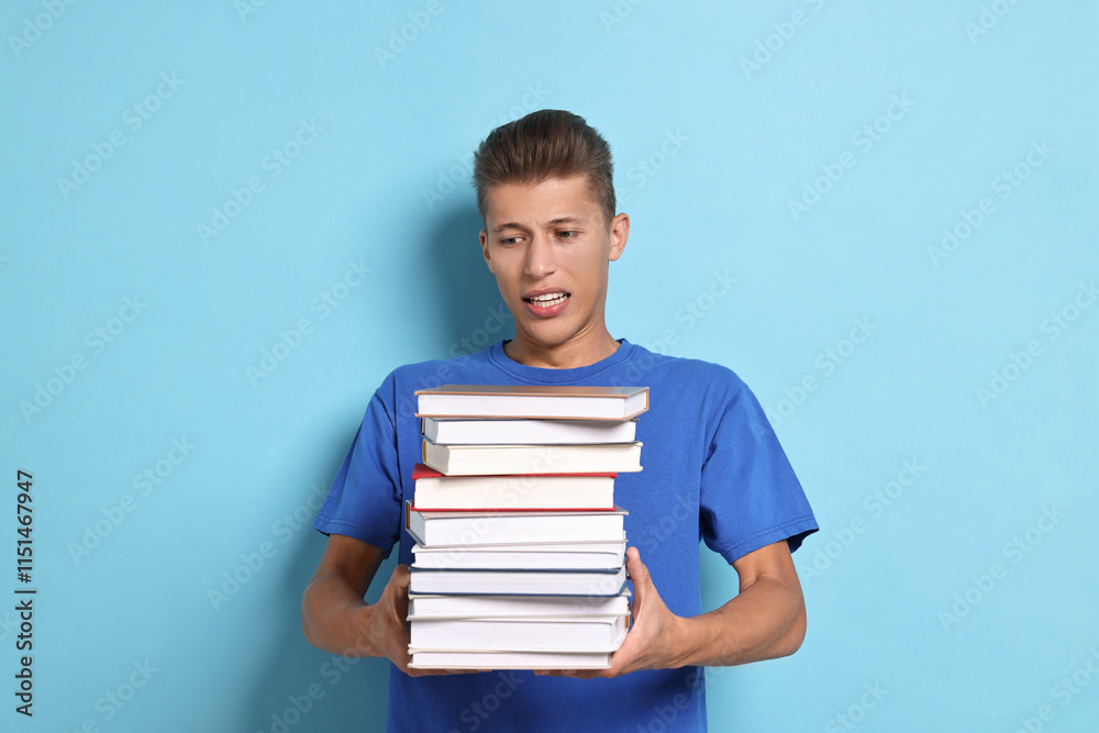 Emotional student with stack of books having stress before exam on light blue background Emotional student with stack of books having stress before exam on light blue background