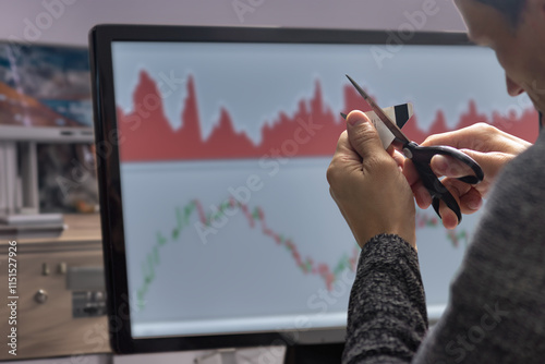 Male stock exchange trader cutting his credit card because of trading mistake. Man trading at home, back view, stock charts on monitor. Beginner in stock exchange part-time job