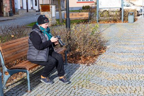Obraz na płótnie A woman with a camera sitting on a bench in an autumn city. w salonie